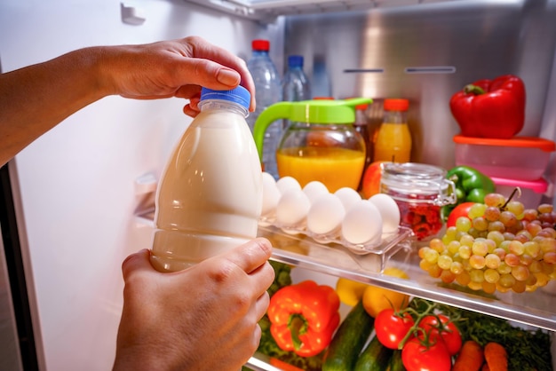 Frau nimmt die Milch aus dem offenen Kühlschrank
