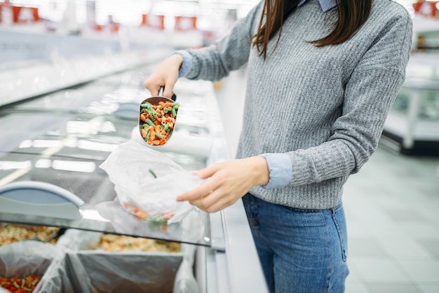 Frau nimmt eine Packung gefrorenes Gemüse in einem Supermarkt, Familieneinkauf. Kundin kauft Produkte im Geschäft, Käufer im Markt