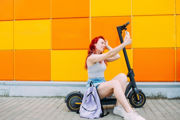 Frau nutzt im Sommer in der Stadt ein Smartphone und einen Elektroroller