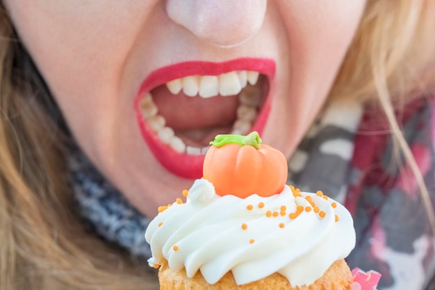 Frau öffnete ihren Mund, um einen Kuchen in Form eines Kürbises zu beißen