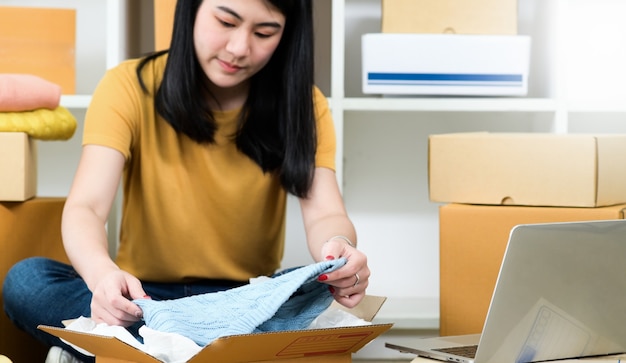 Frau packt ein Hemd in einen Paketkasten zur Lieferung an einen Kunden,Produkte online verkaufen,Pakete transportieren.