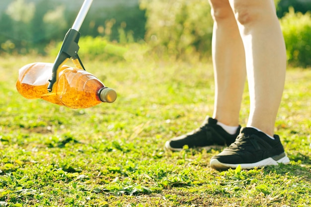 Frau pflückt die Plastikflasche mit dem Müllsammelwerkzeug