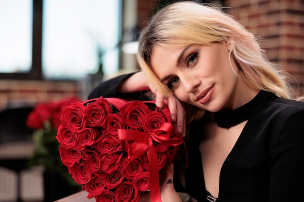 Frau posiert mit roten Rosen Nahaufnahme Porträt, Valentinstag Luxusgeschenk erhalten. Attraktive blonde Freundin mit Blumenstraußkasten, Liebesfeiertagsgruß, Geschenklieferungskonzept