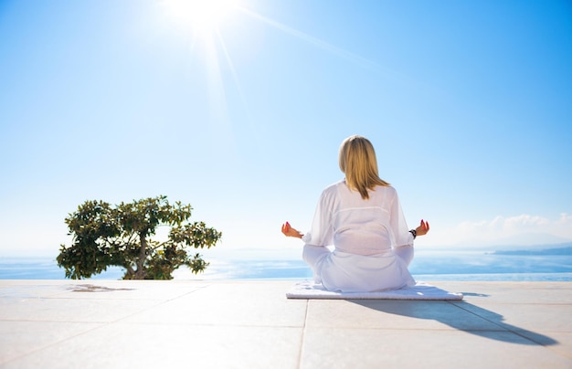 Frau praktiziert Meditation im Freien auf der Terrasse mit wunderschönem Meerblick