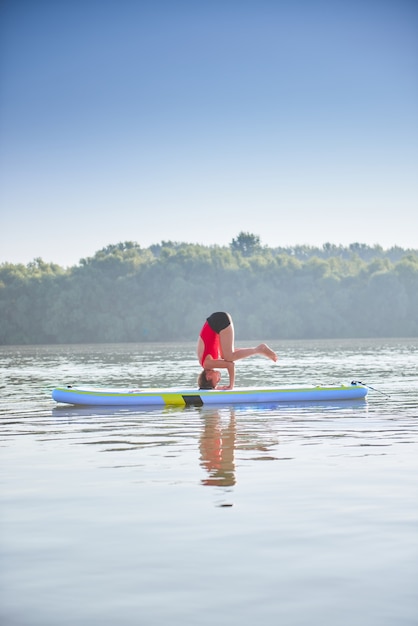 Frau praktiziert Yoga am frühen Morgen auf einem Paddleboard