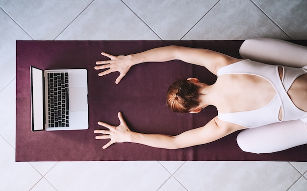 Frau praktiziert Yoga auf Yogamatte mit Laptop Mädchen meditiert mit Videotraining zu Hause