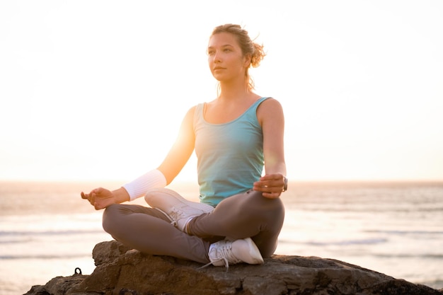 Frau praktiziert Yoga Lotus-Pose zur Meditation mit Sommerferien felsiger Strand Glück und Entspannung Ruhige weibliche Übung mit Yoga meditiert Ozeanstrand mit goldener Zeit des Sonnenuntergangs