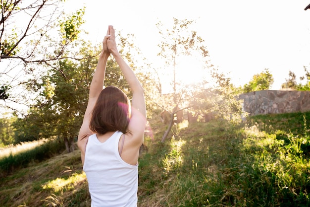 Frau praktiziert Yoga mit erhobenen Armen im Freien im Park