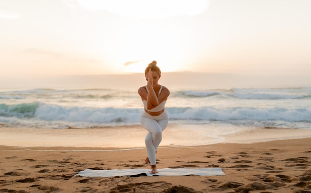 Frau praktiziert Yoga-Pose am Strand bei Sonnenuntergang