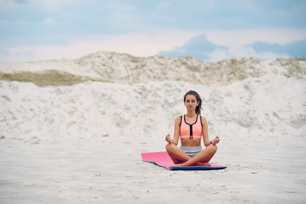 Frau praktiziert Yoga und meditiert im Lotussitz am Strand