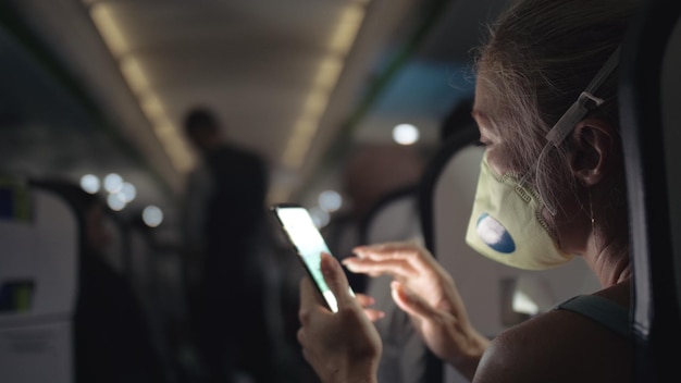 Frau reisen Tourist Kaukasier im Flugzeug mit medizinischer Schutzmaske Lesen Sie Schocknachrichten über Coronovirus auf dem Smartphone