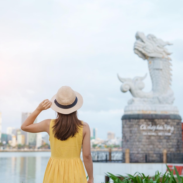 Frau Reisende mit gelbem Kleid zu Besuch in Da Nang Touristische Besichtigung des Flusses mit Karpfendrachenstatue oder Ca Chep Hoa RongLandmark und beliebtem Reisekonzept für Vietnam und Südostasien