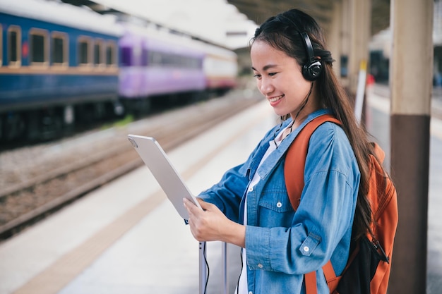 Frau reisender Tourist verwendet Kopfhörer mit Tablet am Bahnhof