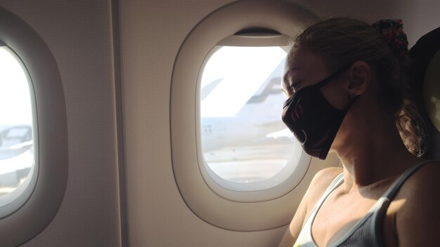Frau reist kaukasisch im Flugzeug mit medizinischer Schutzmaske Touristin im Flugzeug mit Atemschutzmaske Coronavirus covid19