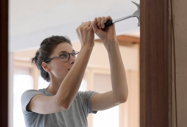 Frau repariert zu Hause eine Tür mit einem Hammer, Hausrenovierungs- und DIY-Konzept