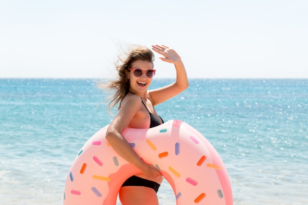 Frau ruft im Meer zu schwimmen und winkt mit der Hand. Mädchen, das auf aufblasbarem Ring am Strand sich entspannt. Sommerferien und Urlaubskonzept.