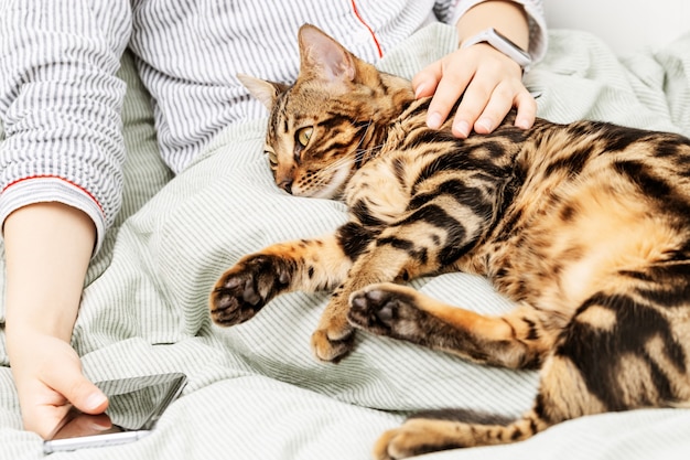 Frau ruht im Bett und Haustierkatze schläft in ihren Armen.