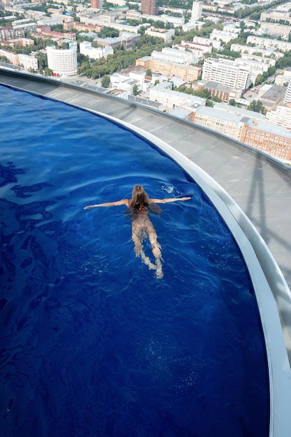 Frau ruht sich im Schwimmbad auf dem Dach über der Stadt aus