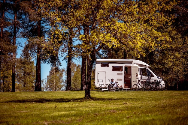 Frau schaut auf den Laptop in der Nähe des Campingplatzes. Wohnwagen Auto Urlaub. Familienurlaubsreise, Urlaubsreise im Wohnmobil RV. Wi-Fi-Verbindungsinformationskommunikationstechnologie.