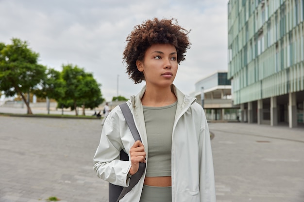 Frau schaut aufmerksam in die Ferne hat regelmäßiges Training trägt Yogamatte und wartet auf Trainer in Sportkleidung in der Stadt