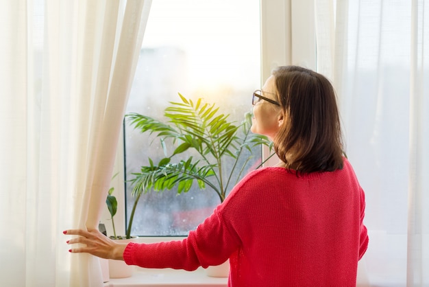 Frau schaut aus dem Fenster, öffnet die Vorhänge