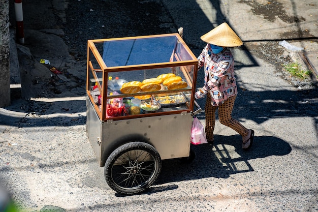 Frau schiebt einen Wagen und verkauft Brot auf der Straße in Vietnam. Straßenverkäufer, die vietnamesisches Brot herstellen