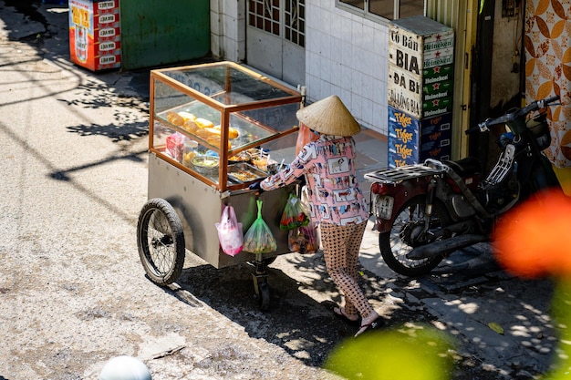 Frau schiebt einen Wagen und verkauft Brot auf der Straße in Vietnam. Straßenverkäufer, die vietnamesisches Brot herstellen