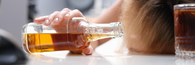 Foto frau schläft am tisch mit einer flasche alkohol in den händen nahaufnahme