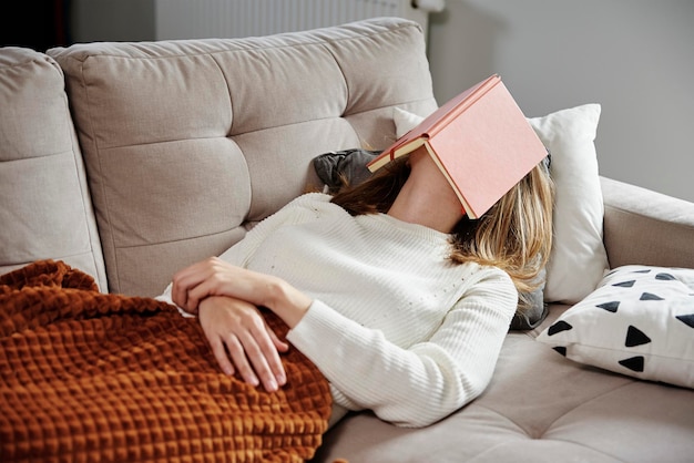 Frau schläft auf Couch mit Buch