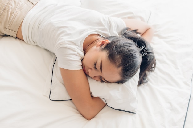 Frau schläft auf ihrem weißen Bett in der Wohnung.