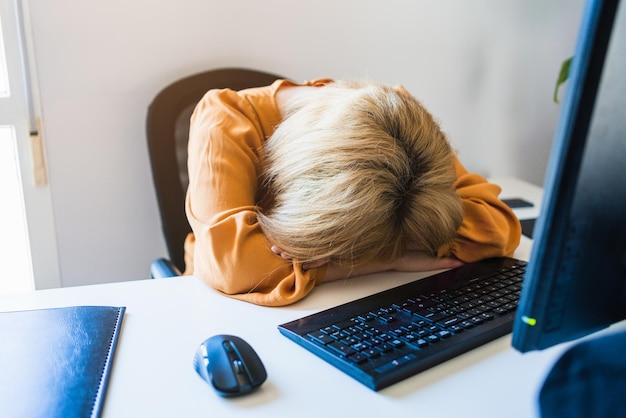 Frau schläft vor dem Computer im Büro