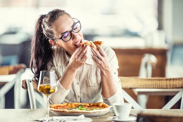 Foto frau schließt die augen, als sie in einem restaurant in ein stück pizza beißt