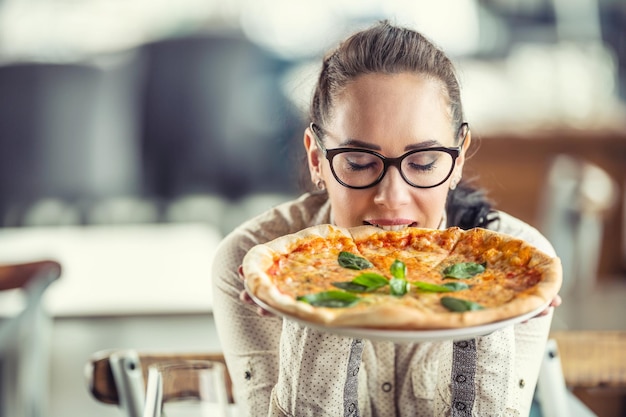 Frau schließt ihre Augen, während sie den Geschmack von frisch gebackener Pizza in ihren Händen genießt