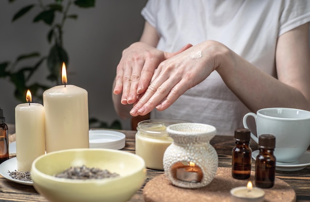 Frau schmiert ihre Hände mit einer natürlichen Bio-Creme, die eine Massage macht Aromalampe mit ätherischen Ölen und Kerzen auf dem Tisch Konzept der Haut- und Selbstpflege in einer Atmosphäre der Harmonie und Entspannung