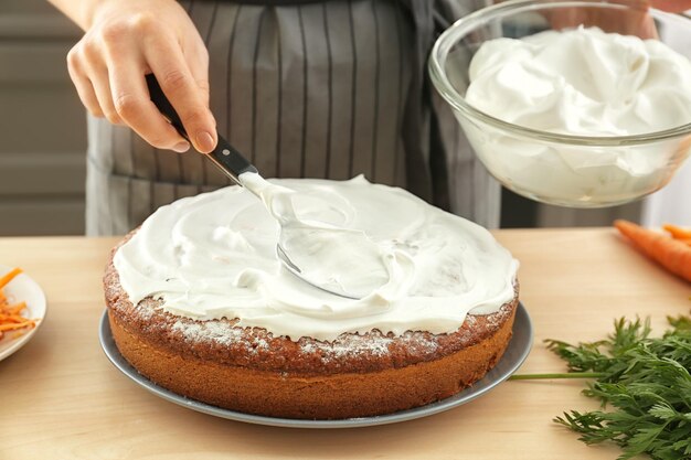 Frau schmiert Sahne auf Karottenkuchen in der Küche