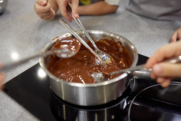 Frau schmilzt Schokolade in einer Pfanne und mischt sie mit Butter, Nahaufnahme. Zu Hause kochen, hausgemachtes süßes Essen.