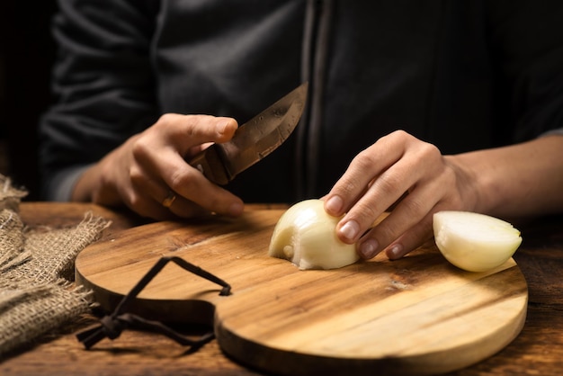 Frau schneidet eine Zwiebel auf einer hölzernen Hintergrundnahaufnahme Vorbereitung für das Kochen