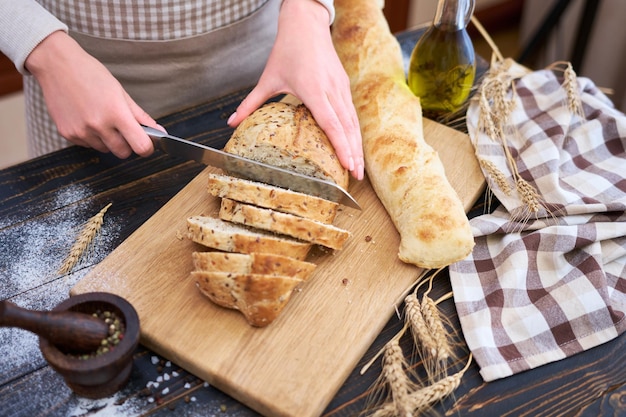 Frau schneidet frisch gebackenes Brot am Küchentisch aus Holz