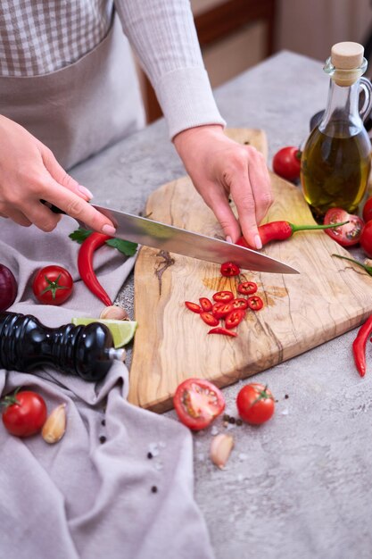 Frau schneidet frische rote Chilischoten Holzschneidebrett in der heimischen Küche