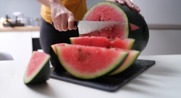 Frau schneidet Wassermelone mit Küchenmesser zu Hause in Nahaufnahme