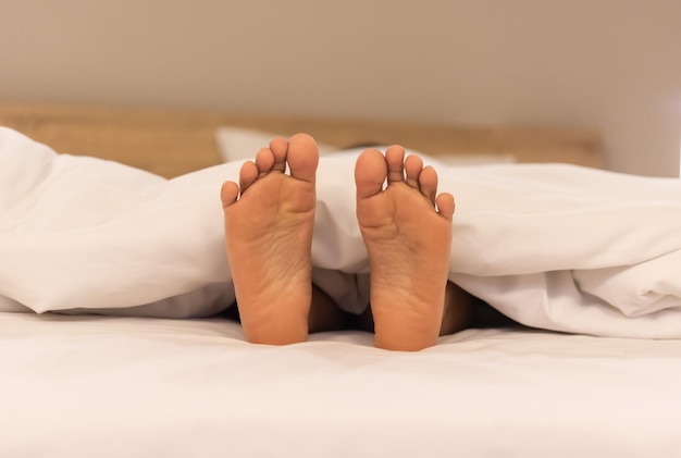 Frau schöne Füße unter weißer Decke auf dem Bett