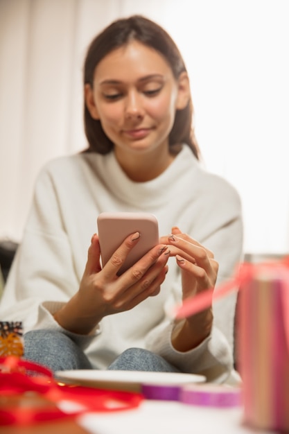 Frau schreibt Nachricht, Grüße für Neujahr und Weihnachten 2021 für Freunde oder Familie mit ihrem Handy. Kontaktaufnahme über Geräte. Feiertage, Feier. Sieht fröhlich, glücklich, vorsichtig aus.