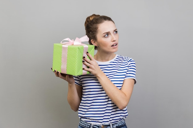 Frau schüttelt eingepackte Geschenkschachtel und ist interessiert, was darin drin ist, und schaut mit neugierigem Gesichtsausdruck weg