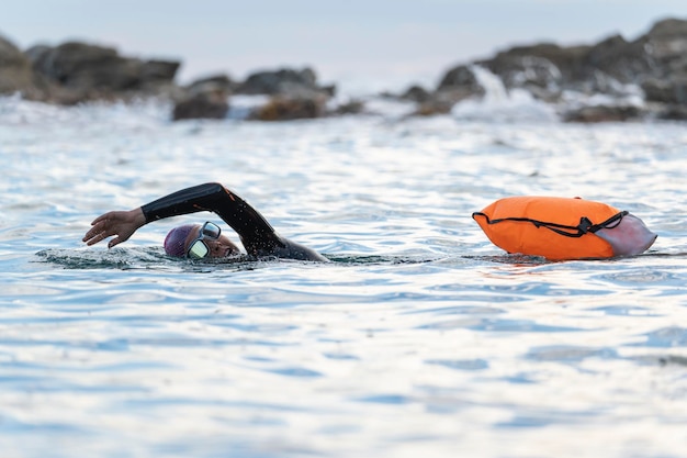 Frau schwimmt im offenen Wasser mit Neoprenanzug und Boje