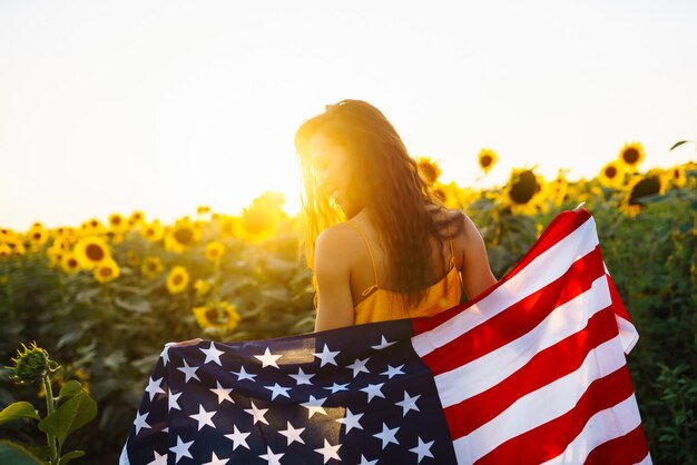 Frau schwingt stolz die amerikanische USA-Flagge auf dem Sonnenblumenfeld. Unabhängigkeitstag, 4. Juli