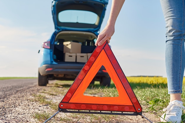 Frau setzt ein Not-Aus-Schild nahe kaputtem Auto auf die Straße