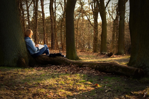 Frau sitzt am Baumstamm im Wald