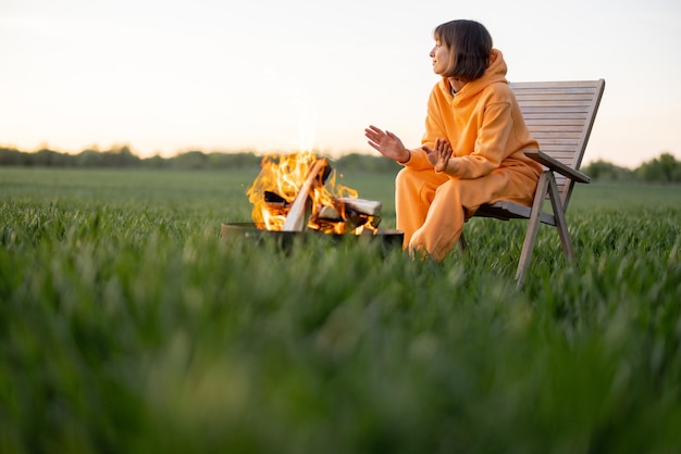 Frau sitzt am Kamin auf der grünen Wiese bei Sonnenuntergang