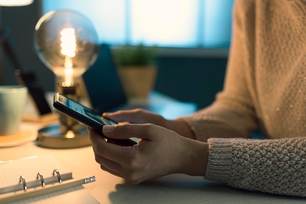 Frau sitzt am Schreibtisch und verbindet sich mit ihrem Smartphone. Sie plant ihre Arbeit mit Online-Apps