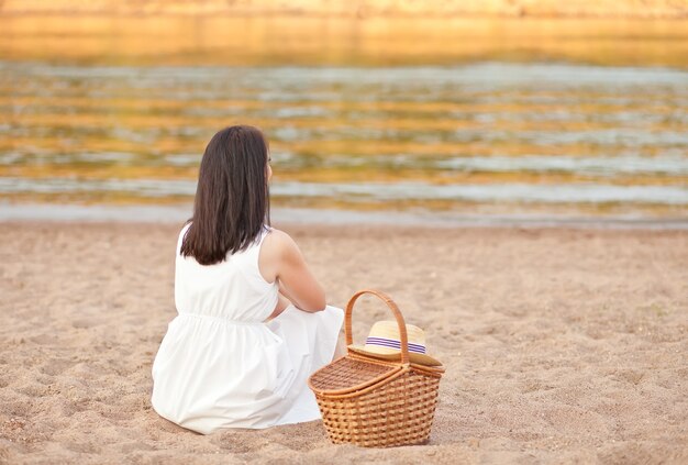Frau sitzt am strand mit picknickkorb